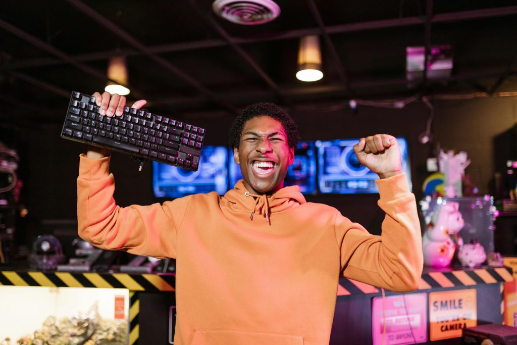 Joyful man in orange jacket celebrating gaming victory with a keyboard.